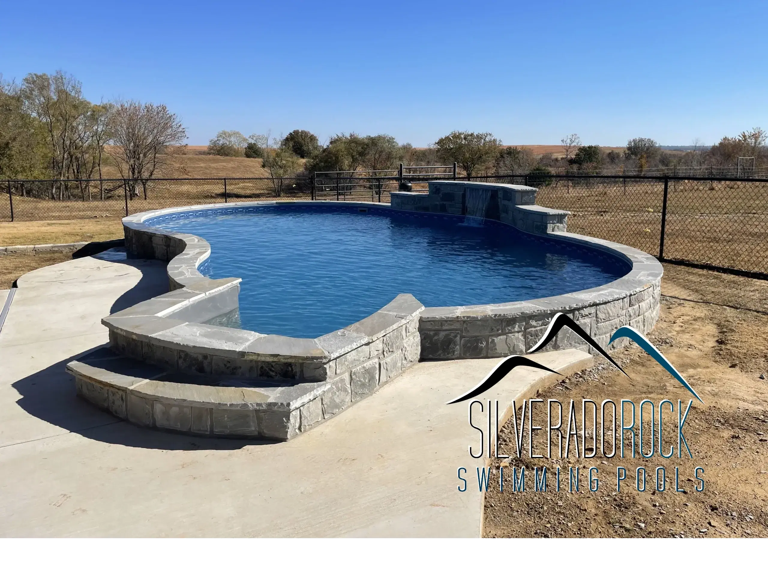 Completed freeform pool with stone surround and concrete steps installed in Tulsa, OK