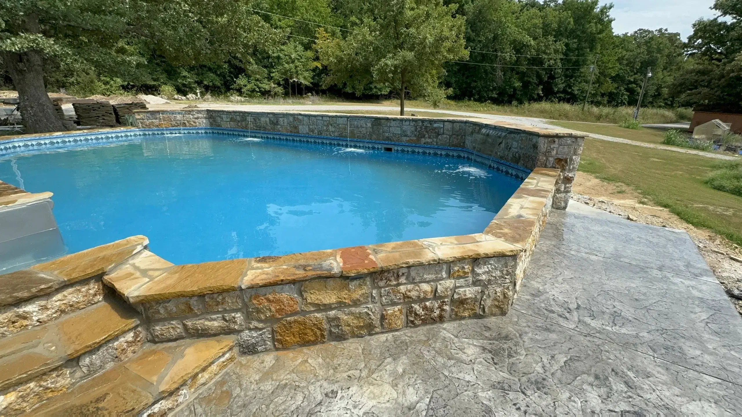 Completed rectangle pool with natural rock surround and stamped concrete decking — Tulsa, OK